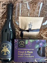 Load image into Gallery viewer, A gift basket arrangement in a straw-lined box featuring a Black Grape Society wine bottle, a bag from wild jennel co., and a purple box of Broughton &amp; Meyer Entertainers Selection Pinot &amp; Plum Fruit Paste with Crackers.

